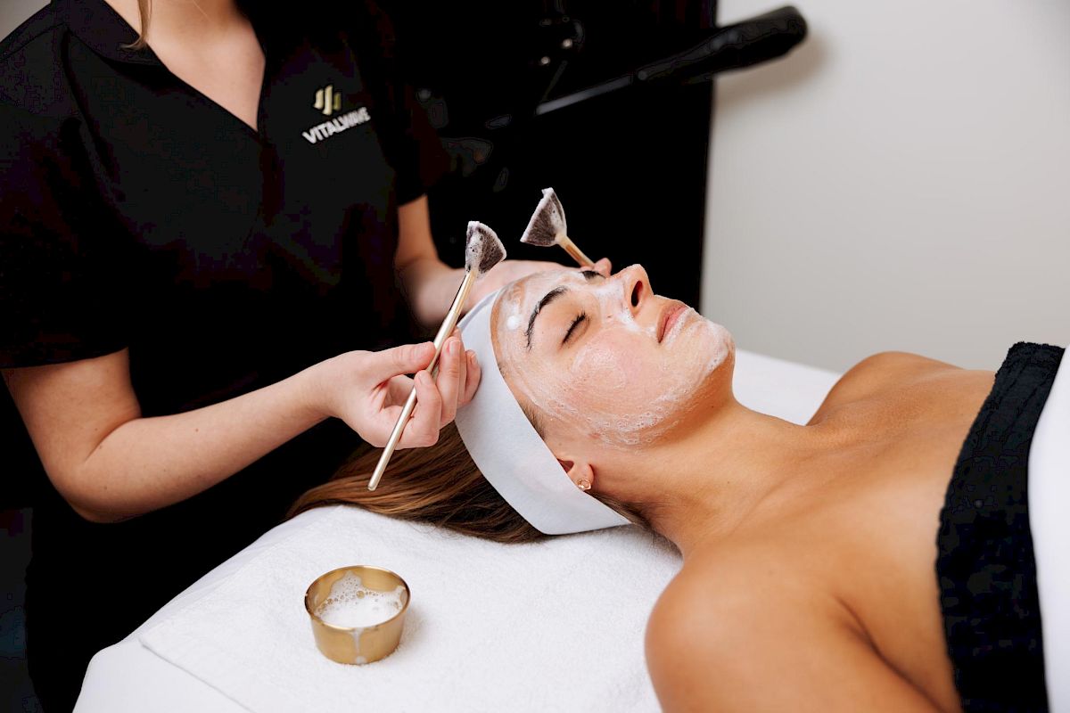 Esthetician at VitalWave in Greenville, South Carolina applying a white enzyme mask to a client's face with a treatment brush