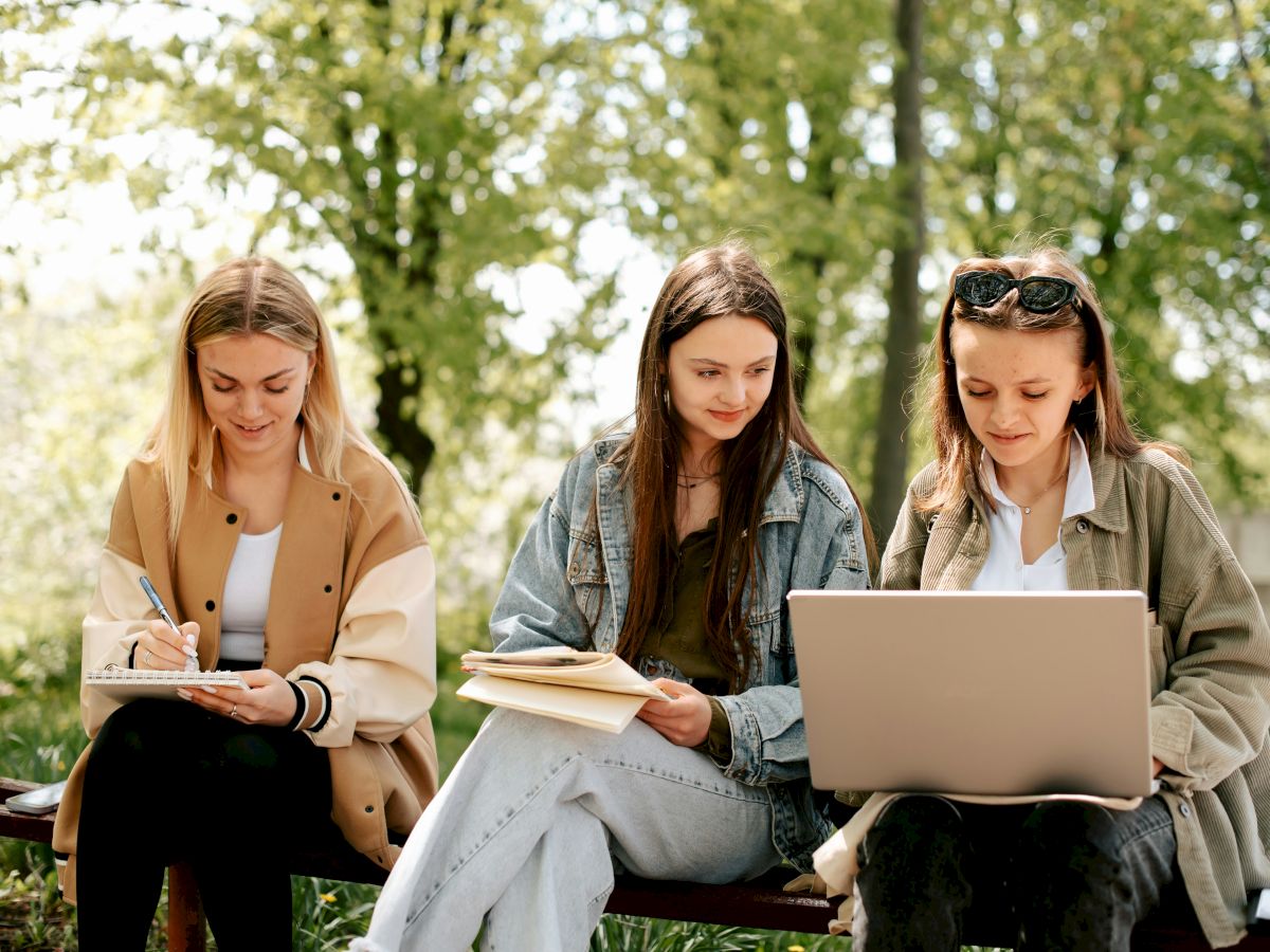 Three women studying outdoors in a park on a sunny day